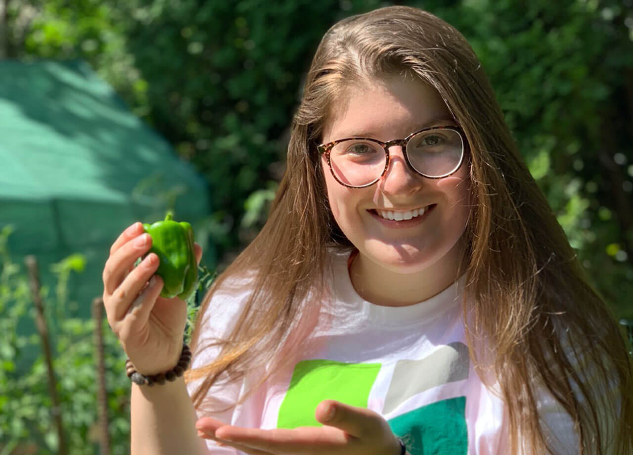 Anna Ciacciarella smiles as she holds up a pepper in a field