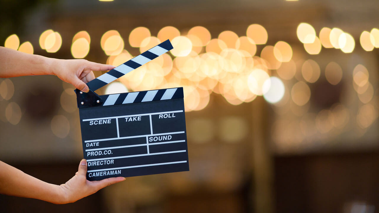 Hands holding a film slate with gold lights in the background.