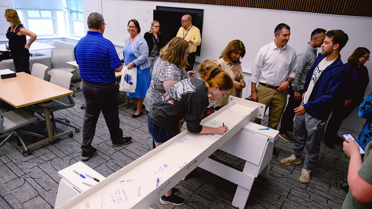 lauren jerram, a redhaired female business student, leans over the beam to sign it and leave a note