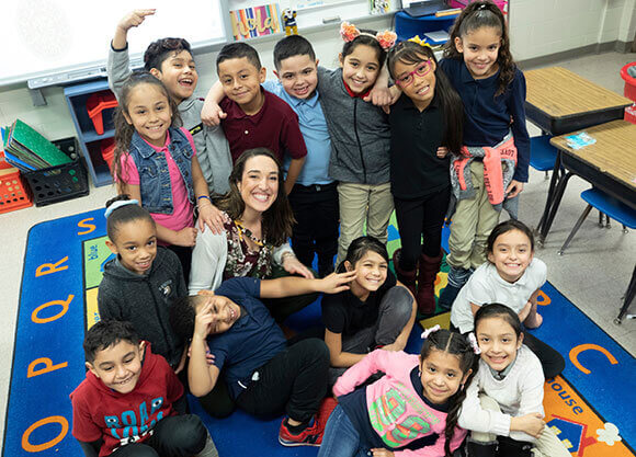 Erin Westerman sits on a colorful rug in her classroom surrounded by her third grade students.