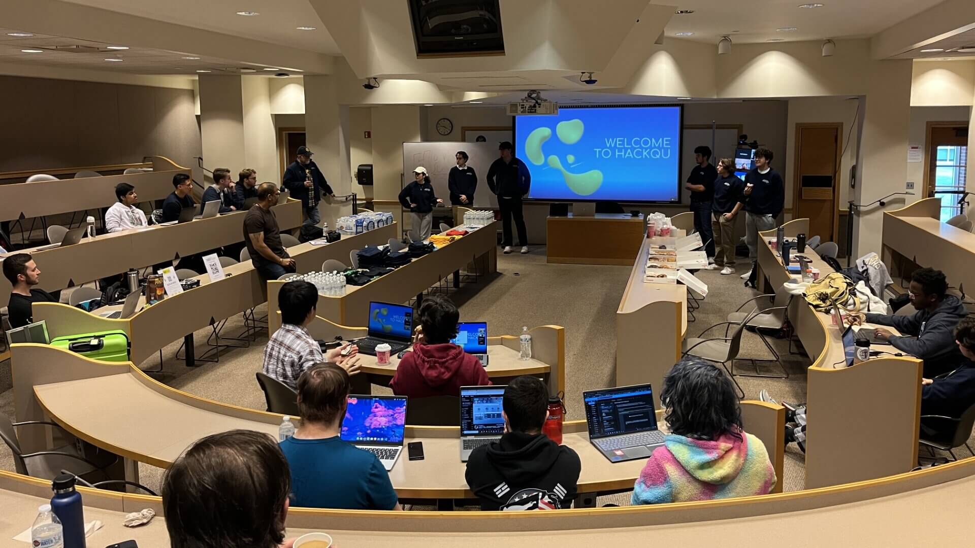 Room full of students with open laptops watch the presenters at the front of the classroom