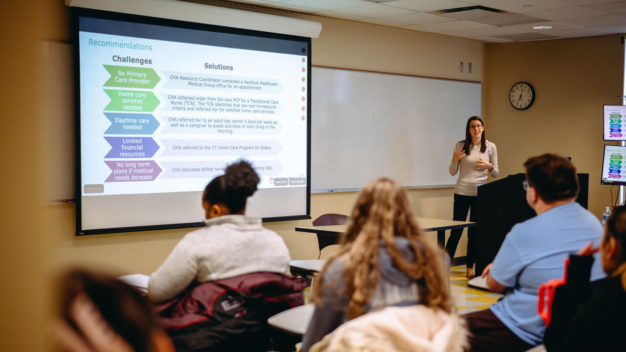 Jennifer McCaughey presents to a class next to a whiteboard.