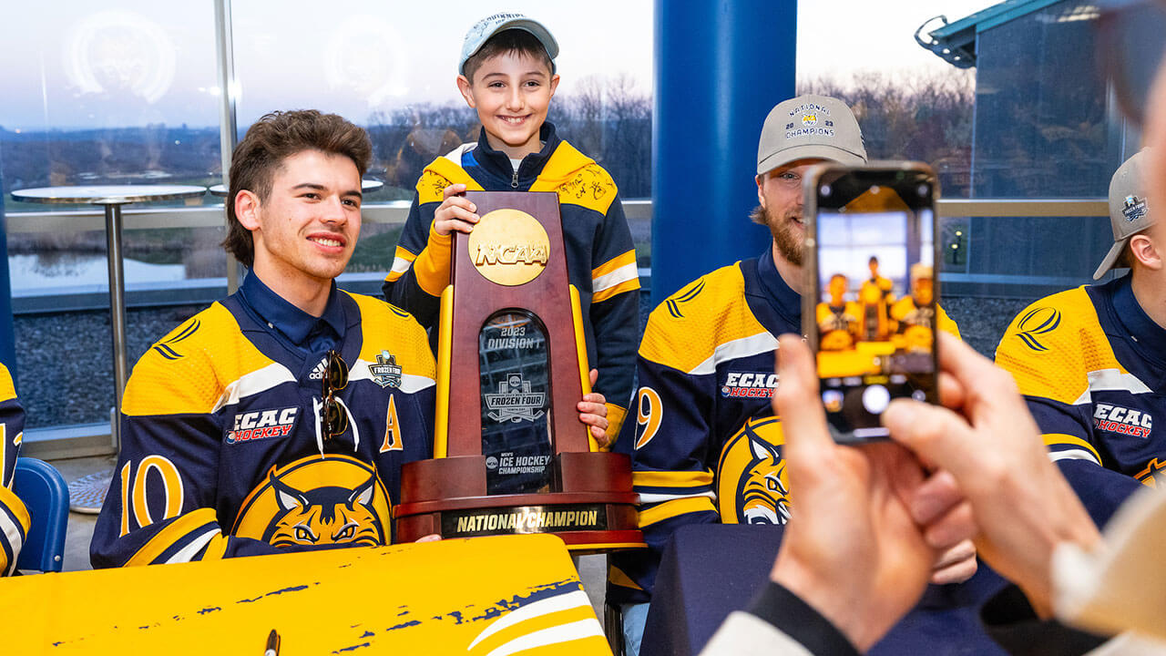 A men's ice hockey player takes a photo with a fan