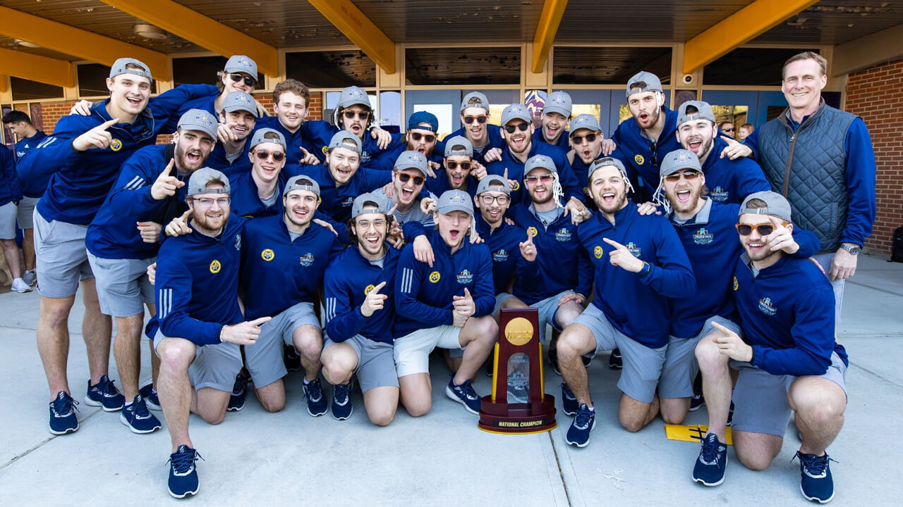 Men's ice hockey team members and coach pose and cheer with the national champions trophy