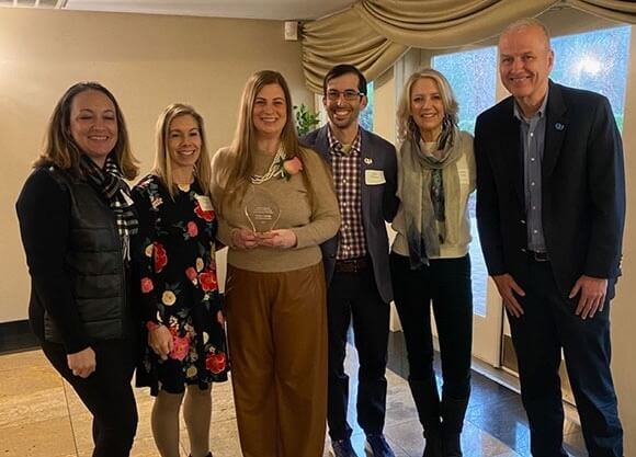 A group photo of Natale smiling holding her award with other individuals.