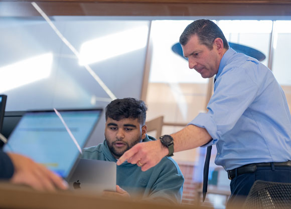 A professor shows a student something on their laptop during class.