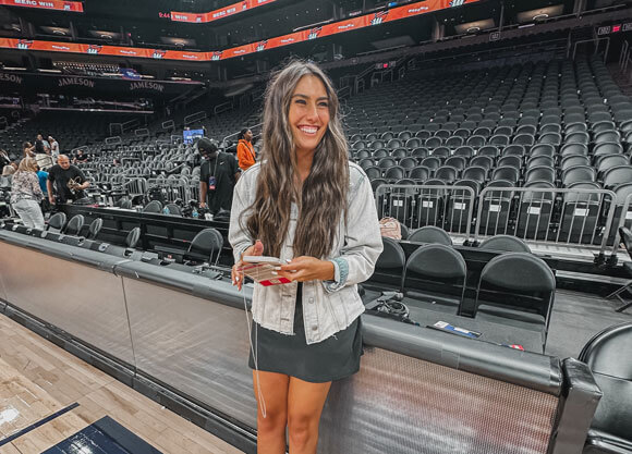 robyn brown poses on the side of a basketball court in front of the stadium seats