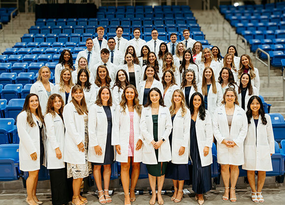 Physician assistant students receive their long white coats and smile for a photo.