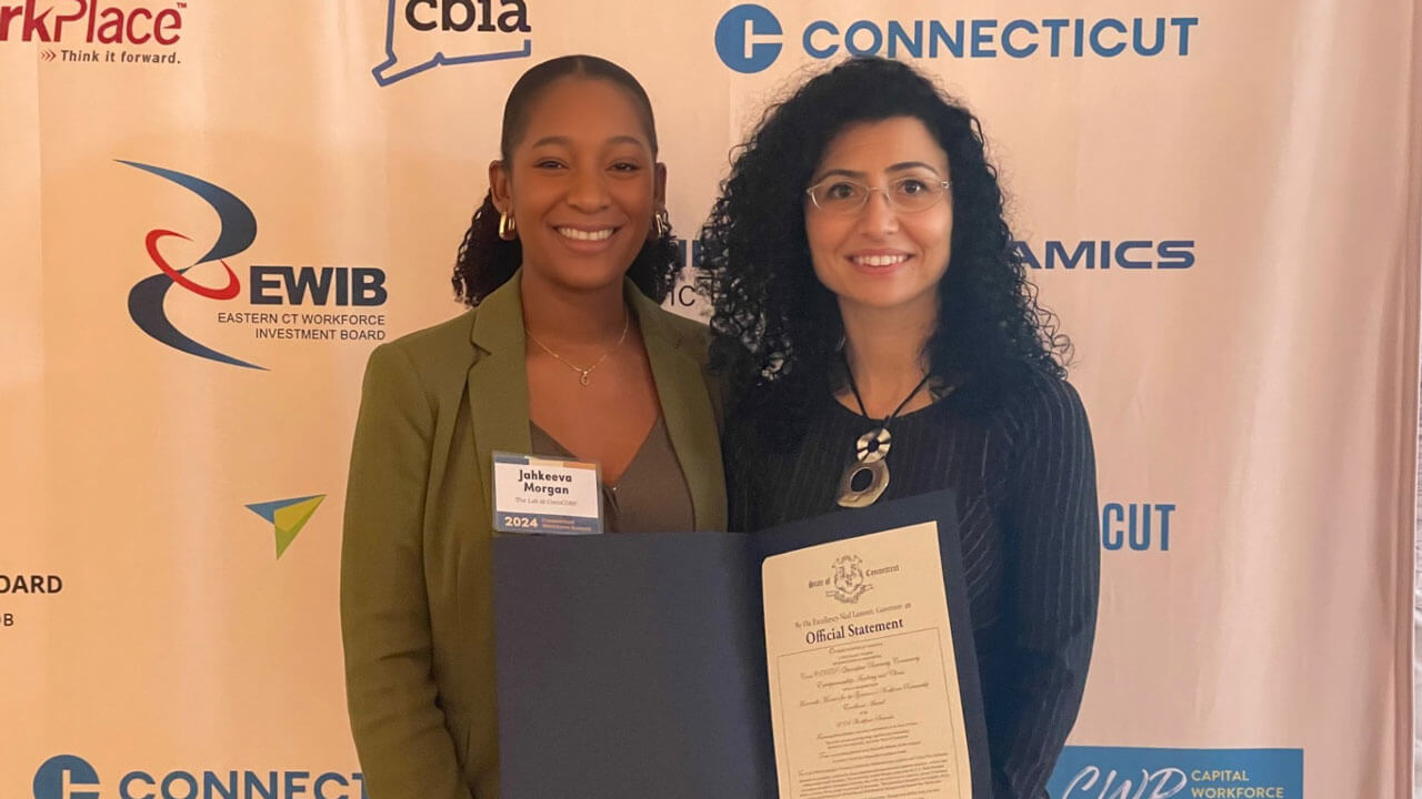 Director of the ConnCORP/QU Community Entrepreneurship Academy and Clinics, Tuvana Rua, smiles with award in front of background