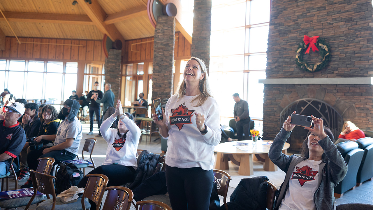 A fan stands in Rocky Top Student Center, cheering while watching results on a screen.