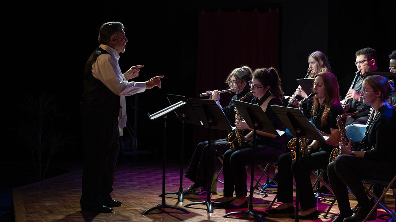 A conductor stands in front of students holding musical instruments as they perform their concert.