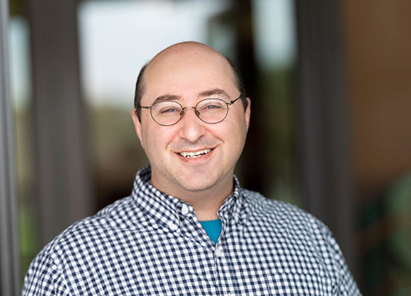 Adam Weinstein smiling in a blue and white button up shirt