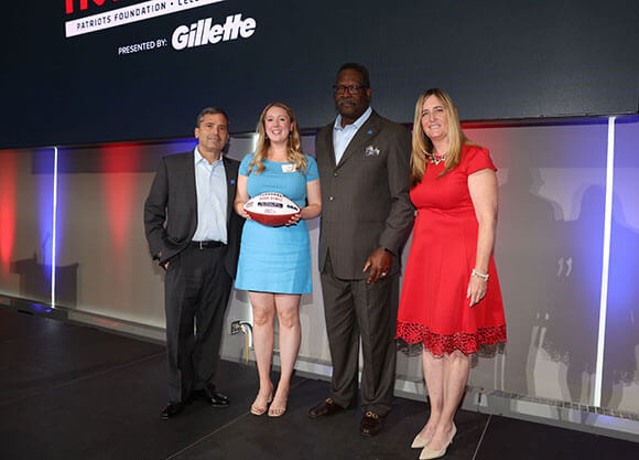 Bobbi Dynice poses onstage with Kraft Family and New England Patriots Foundation while holding award