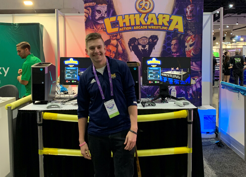 Alumni Chad Reilly standing in front of a booth at a gaming convention