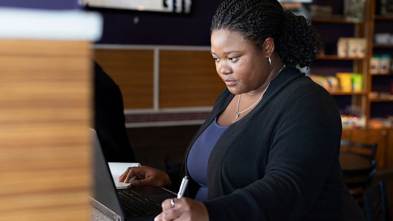 woman writing resume at desk in front of a laptop