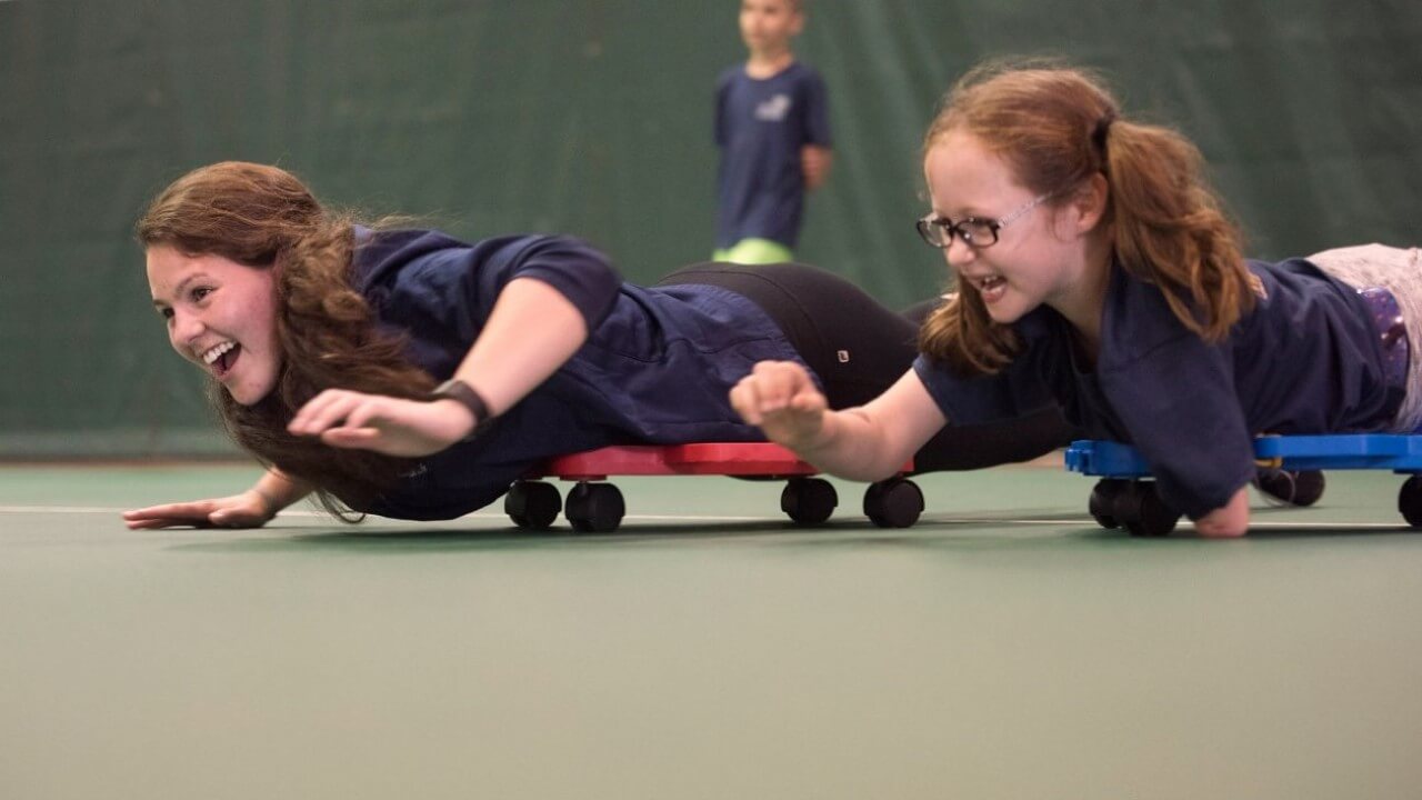 Quinnipiac graduate occupational therapy student and child play on scooter boards at camp.