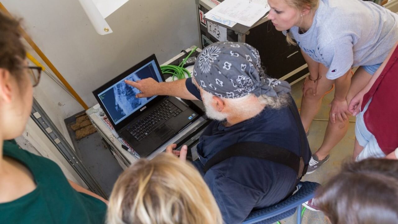 A professor and students examine a coffin scan on a computer.