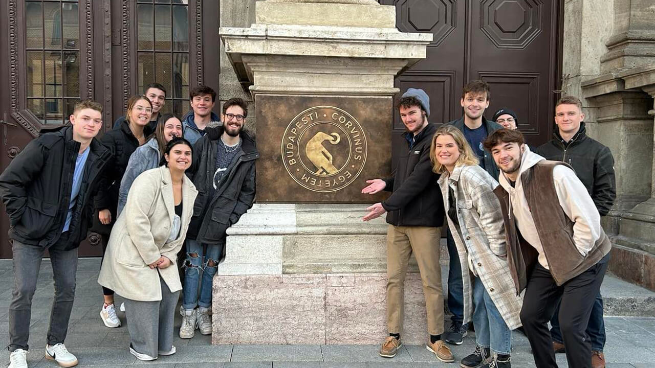 A group of student posing in front of Corvinus emblem