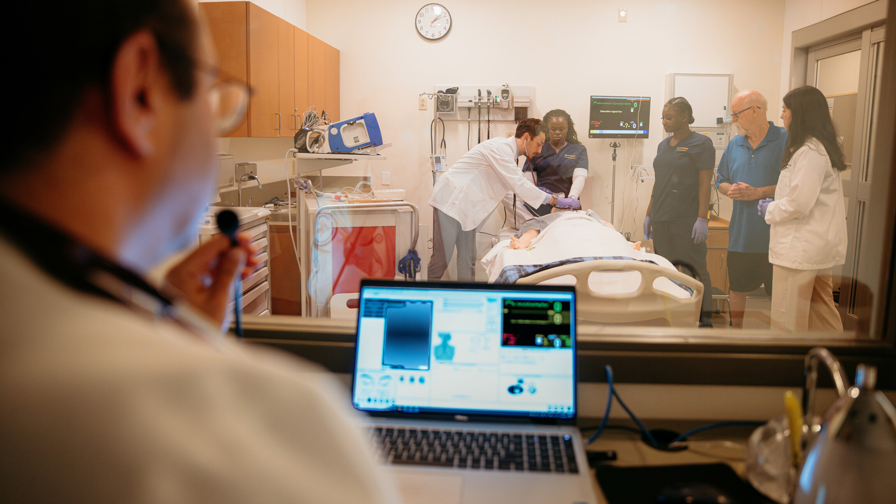 A health sciences professor gives direction to students performing a procedure in the simulation suite