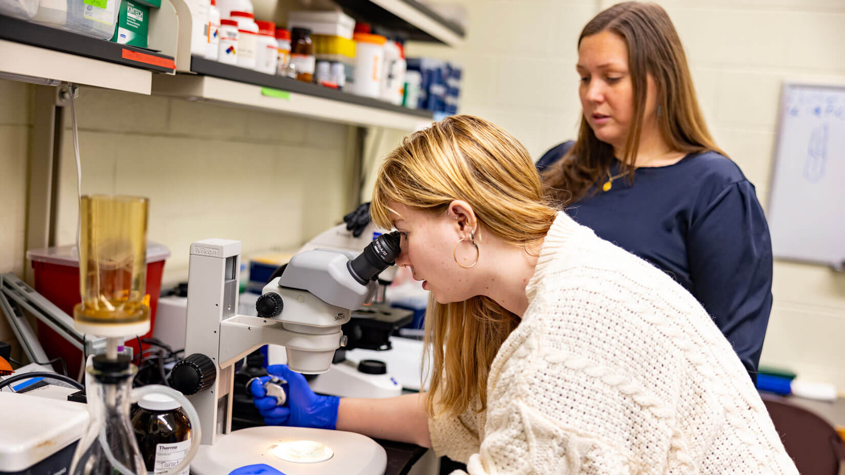 A student and her professor examine a specimen under a microscope.