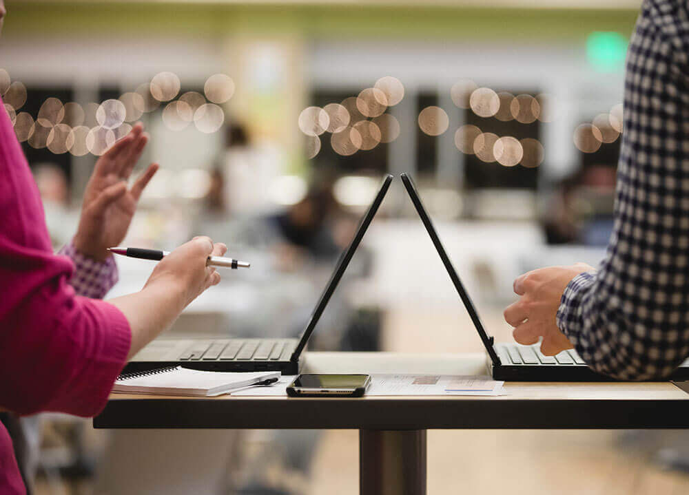 Close up shot of two laptops back-to-back with people's arms gesticulating toward one another