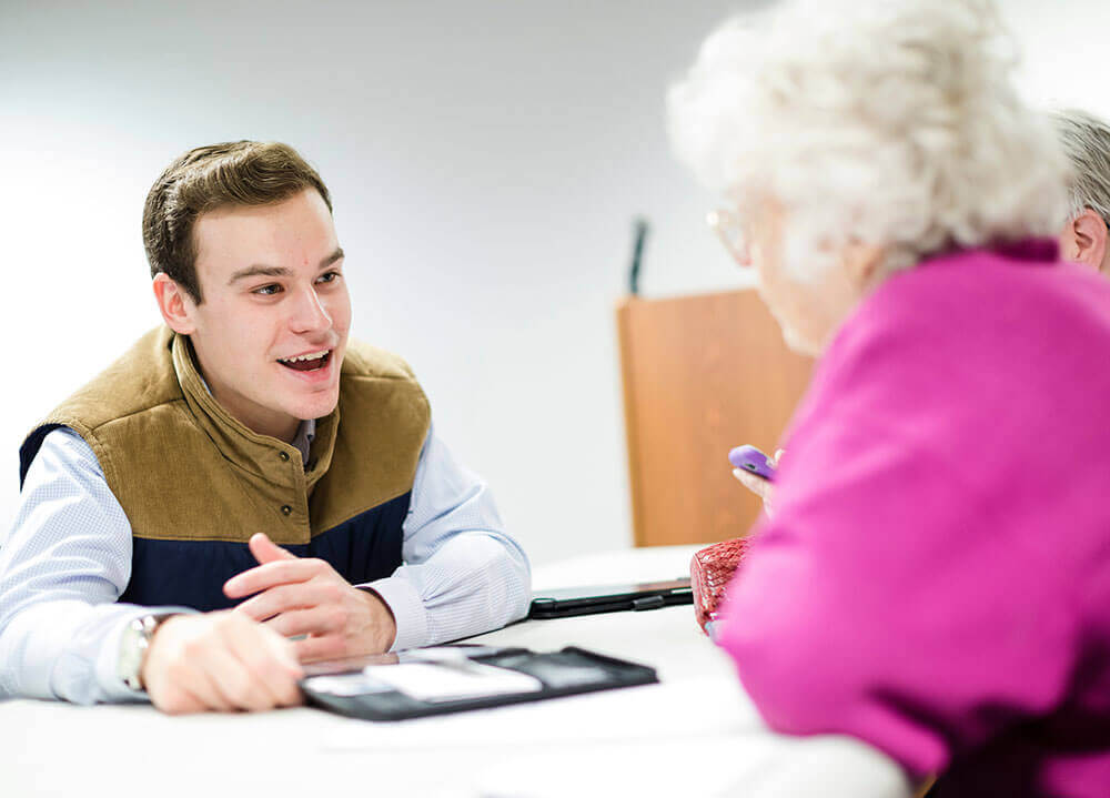 A Quinnipiac student demonstrates how to use a tablet and mobile phone to two senior citizens during a workshop