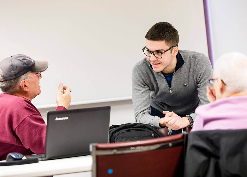 A student speaks with two senior citizens during a technology workshop