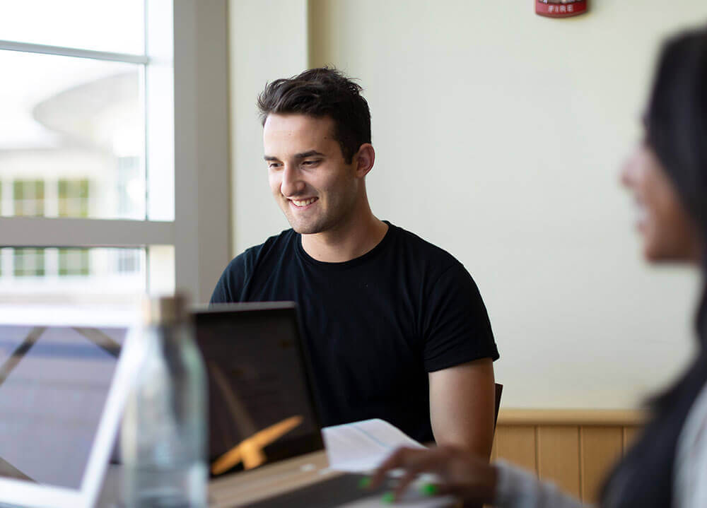 A student starts out a window with his laptop sitting in front of him