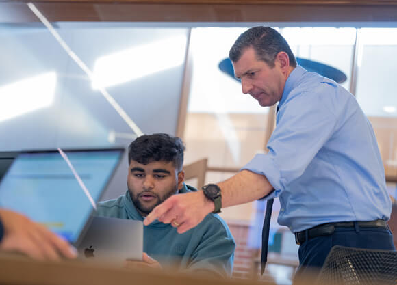 A male professor looking at a male student's laptop