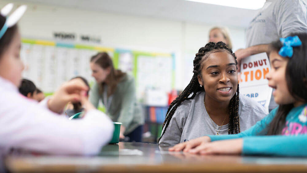 A business student smiles while talking to an elementary schooler