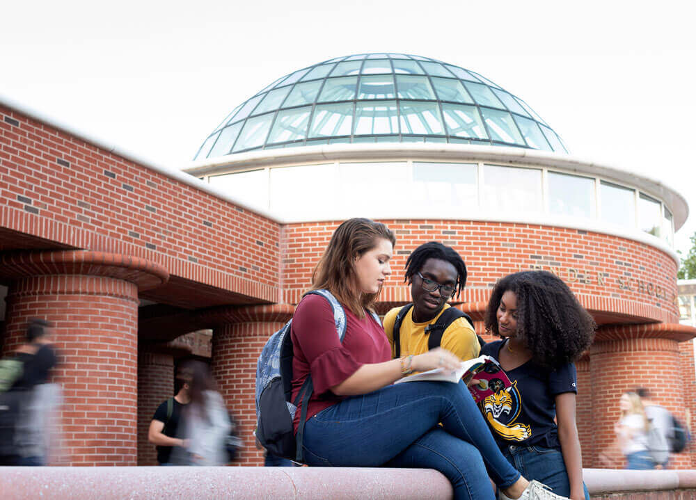 Three students sit outside in front of the Lender School of Business