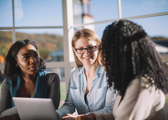 Three students sit at a table in front of a laptop