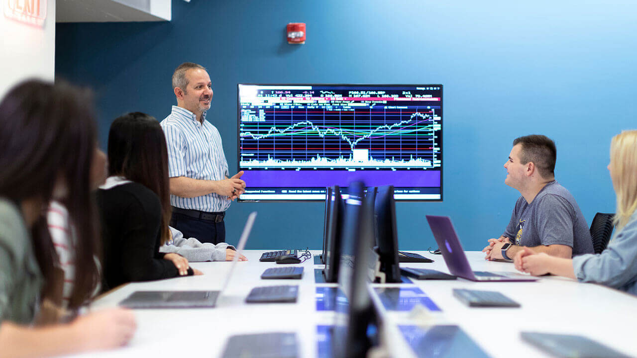 A business professor points at financial figures on a monitor in class