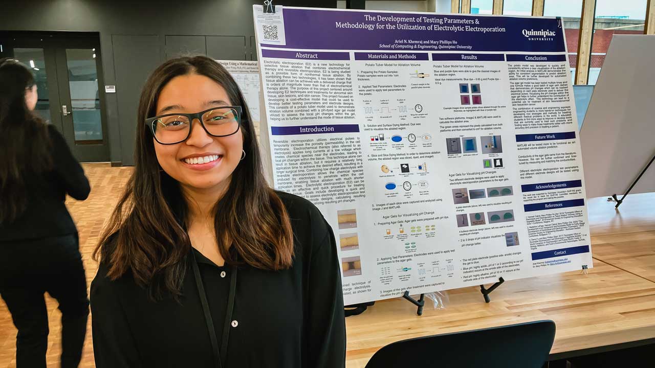 Ariel Khemraj posing in front of her poster titled "The Development of Testing Parameters & Methodology for the Utilization of Electrolytic Electroporation"