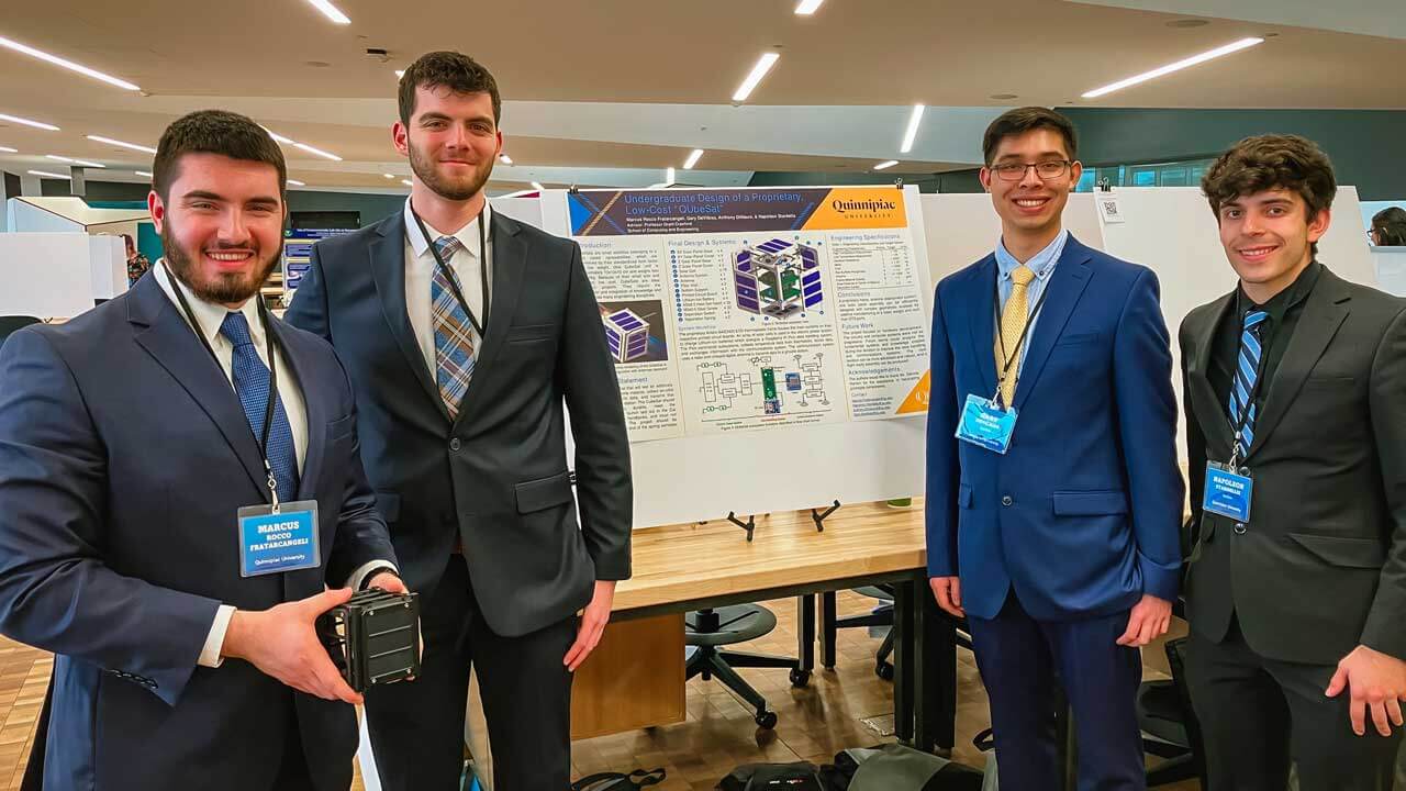 4 male students posing in front of their poster detailing "QUbeSat"