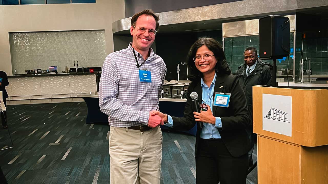 A male professor accepting a paper award from a woman.