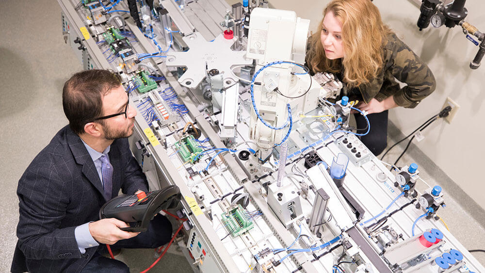 Birds eye view of a large machine with a professor showing a student how it works