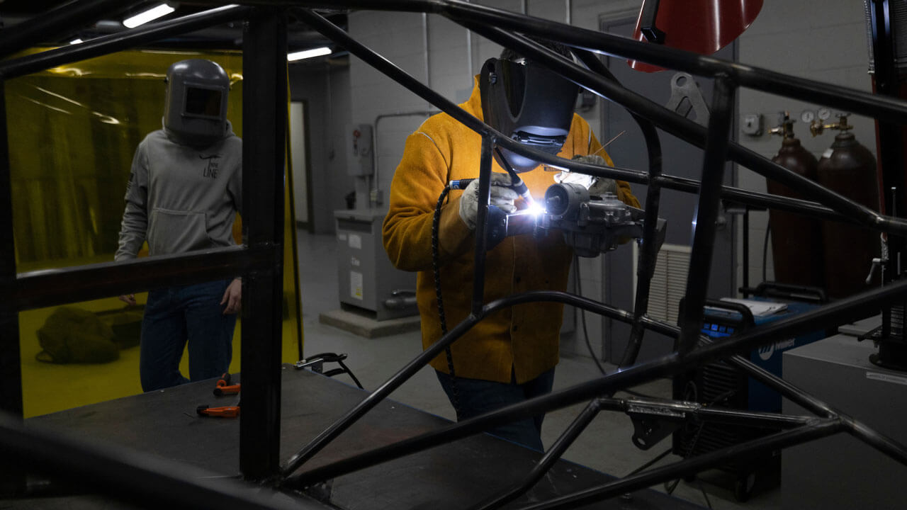 A student wearing a face shield while holding a laser on the equipment.