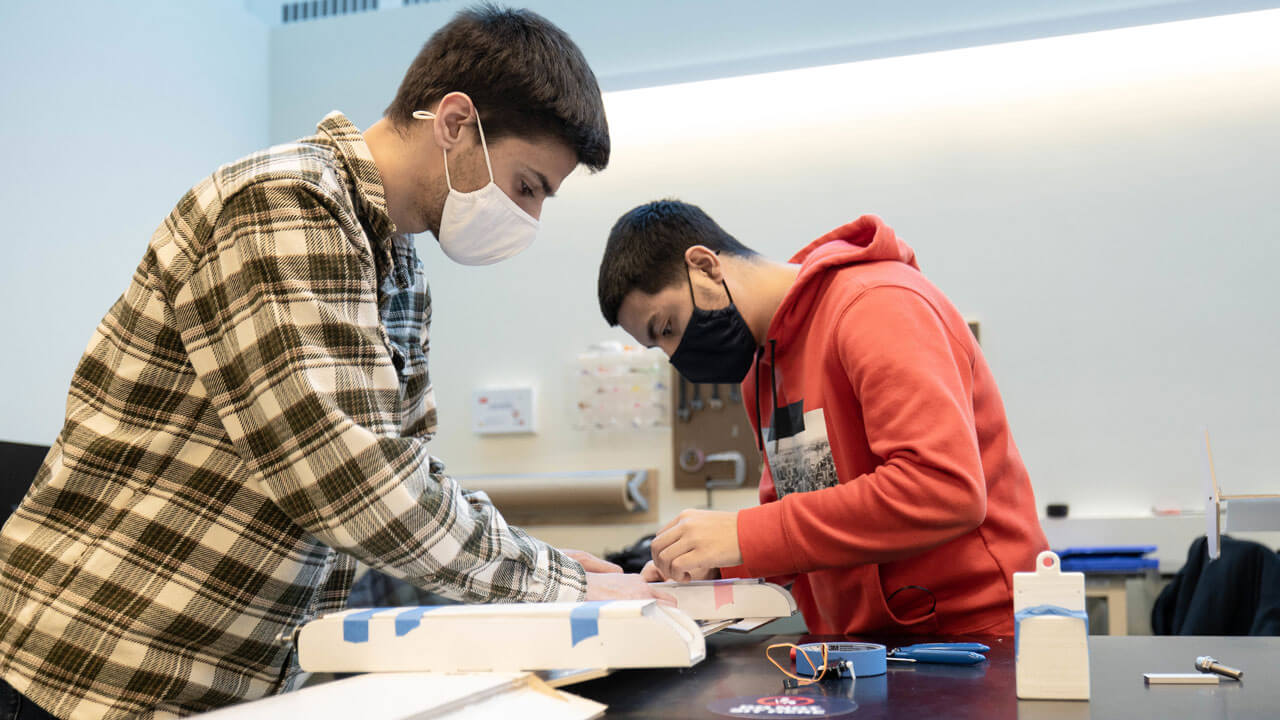 School of Engineering students Ethan Moriarty and Seth Cornier placing tape on wood pieces.