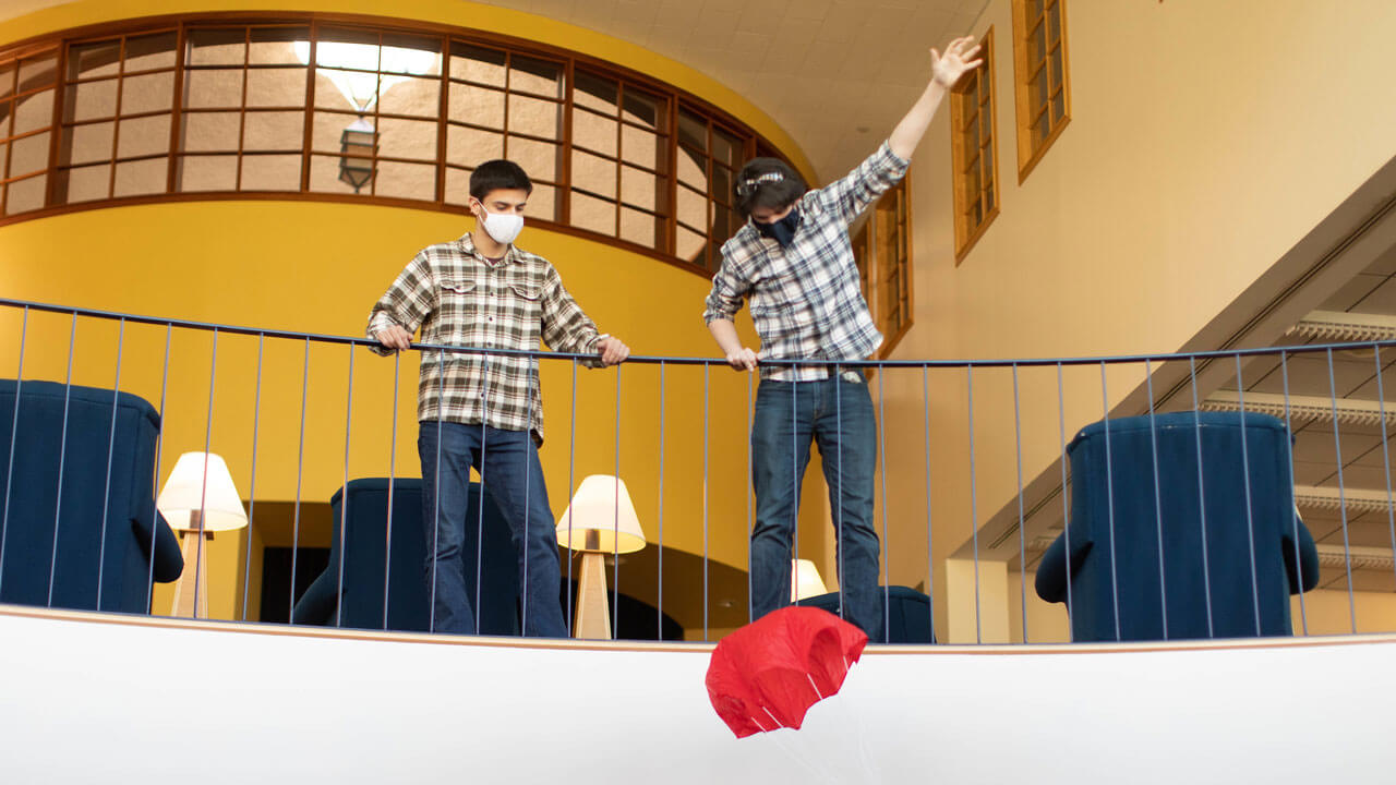 Two students stand at a banister while watching a parachute fly down.