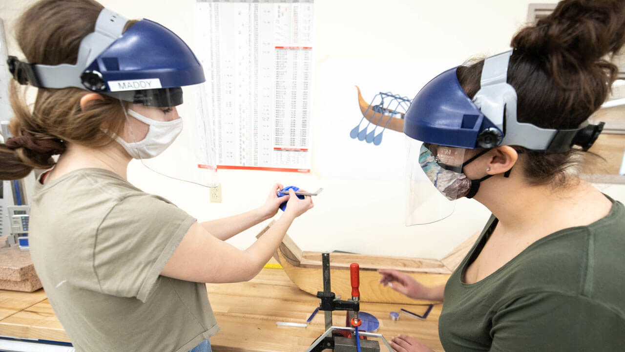 School of Engineering students Madeline LePage and Gabriella Ambery work on their senior projects while touching a piece of wood on a table.