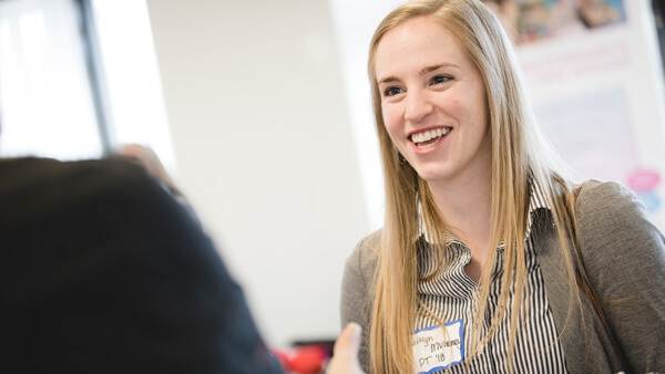 A student holds her notebook while talking to a job recruiter at a career fair