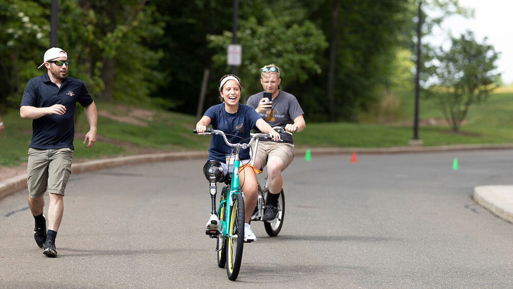 Two health sciences students assist a teen with limb loss riding a bicycle