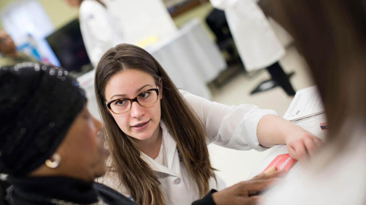 Professor sits at a table and speaks with a patient at the health fair