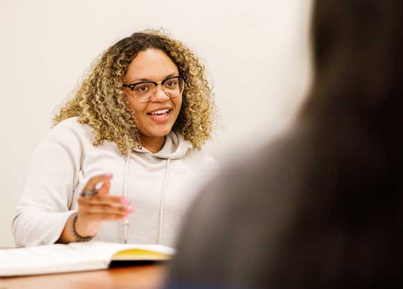 A female student sitting at a table speaking to someone