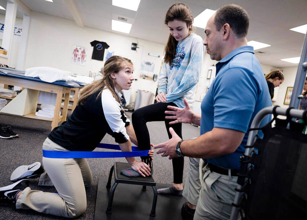 A student intern works with a patient while being advised by the owner of the practice