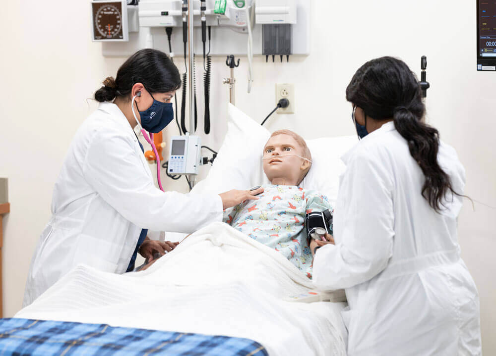 Two accelerated nursing students practice clinical skills with a mannequin