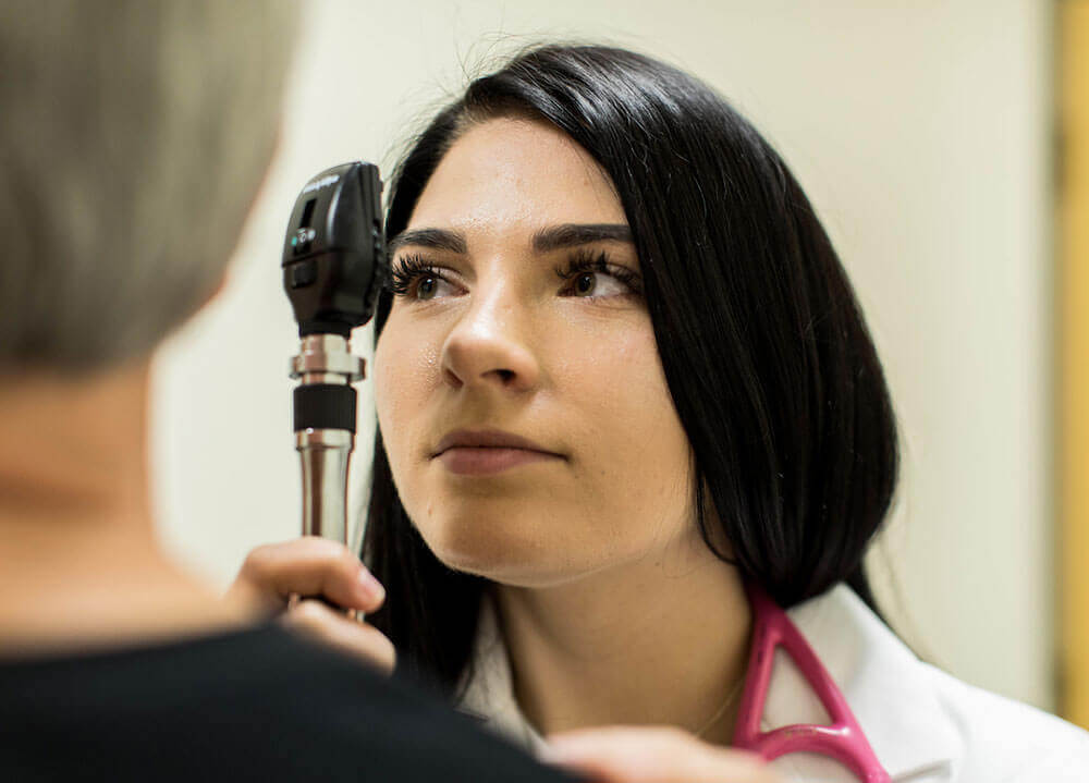 A nursing student uses a light to examine the eyes of a patient