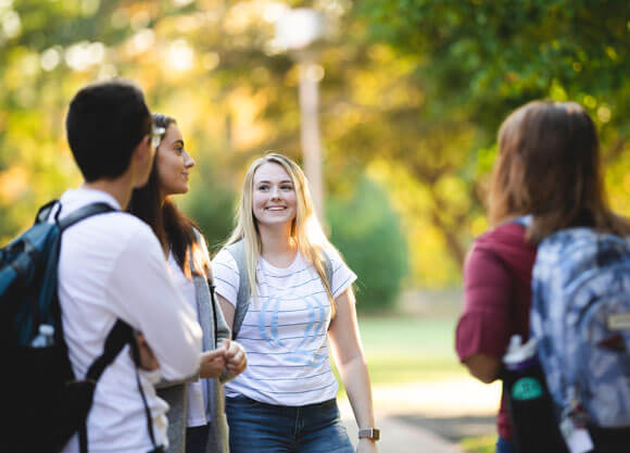 Half a dozen students talk outside amongst fall foliage