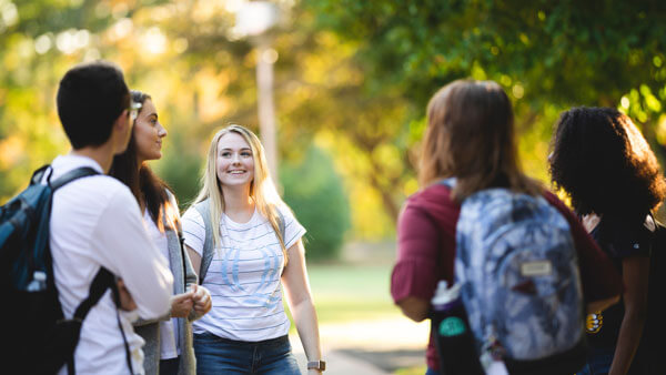 Half a dozen students talk outside among fall foliage